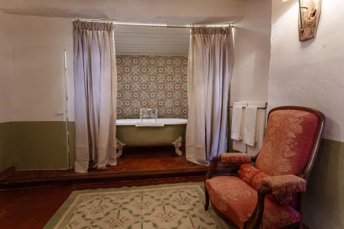 Badezimmer in der Ambre Suite der La Bouscatière mit freistehender Badewanne, Lavendelvorhängen und Vintage-Sessel.