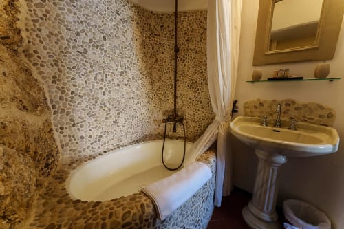 Elegantes Badezimmer mit Kieselsteinfliesen an den Wänden, ovaler Badewanne, Spülbecken auf Sockel und Flussblick im Zimmer Lula von La Bouscatière,
