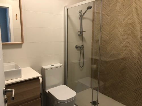 Baño moderno con ducha tipo walk-in en la villa Casa Arealonga de Vigo con azulejos blancos y puerta de cristal en espiga