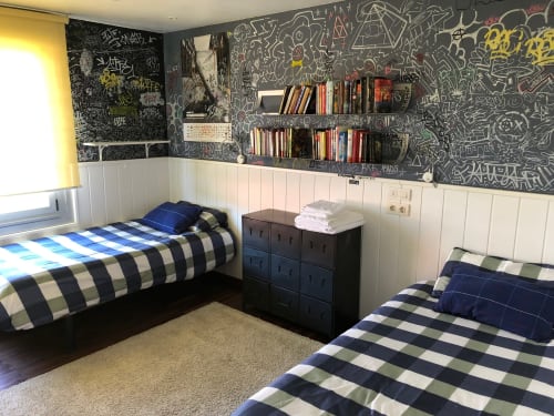 Moderno dormitorio de la villa Casa Arealonga en Vigo con dos camas individuales, pared de pizarra, estanterías integradas y ropa de cama a rayas.