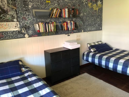 Dormitorio compartido en villa Casa Arealonga, Vigo: dos camas individuales, ropa de cama a cuadros y estanterías empotradas sobre arte callejero