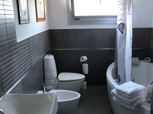 Baño moderno con paredes de azulejos oscuros, inodoro, bidé y ducha en la villa Grila House de Casa Arealonga en Vigo