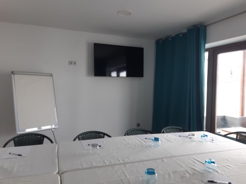 Moderna sala de conferencias de Casa Rural La Perla con mesa larga, sillas, pantalla TV y cortinas turquesas en Hiendelaencina