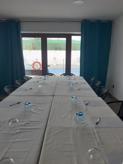 Sala de conferencias de Casa Rural La Perla con mesa larga, vasos de agua y vista a la terraza en Hiendelaencina