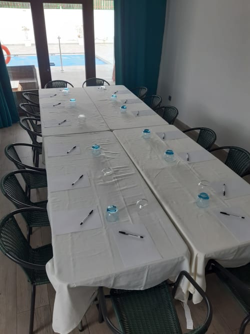 Sala de conferencias en Casa Rural La Perla con mesa vestida de blanco, sillas negras y vasos de agua en Hiendelaencina