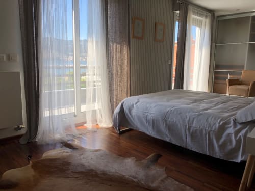 Espacioso dormitorio en Casa Arealonga de Vigo con ventanales panorámicos, ropa de cama azul, suelos de madera y vistas a la ciudad