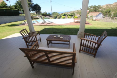 Muebles de madera y mesa en terraza cubierta con vistas a la piscina y jardines del hotel A Ballenera de Caneliñas en Cee
