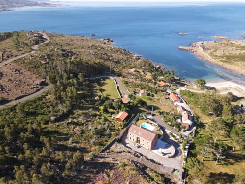 Vista aérea del hotel A Ballenera de Caneliñas en Cee, Galicia, con acantilados costeros, mar azul y edificios dispersos