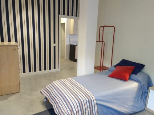 Dormitorio moderno en Casa Arealonga, Vigo con ropa de cama azul, almohada roja, pared divisoria a rayas y mobiliario minimalista
