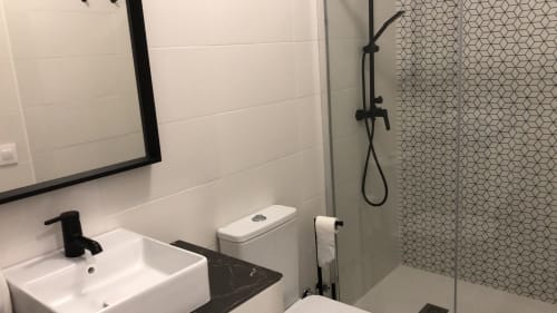Baño moderno del hotel Casa Arealonga en Vigo con azulejos blancos estilo metro, accesorios negros y ducha con patrón geométrico