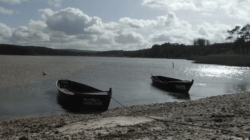 Dois barcos de pesca ancorados em águas tranquilas perto de Óbidos, Portugal, com margens florestadas e céu nublado