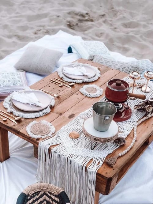 Espaço de refeições à beira-mar em Kindnessmoon em Óbidos com mesa de madeira, lençol branco e decoração boho