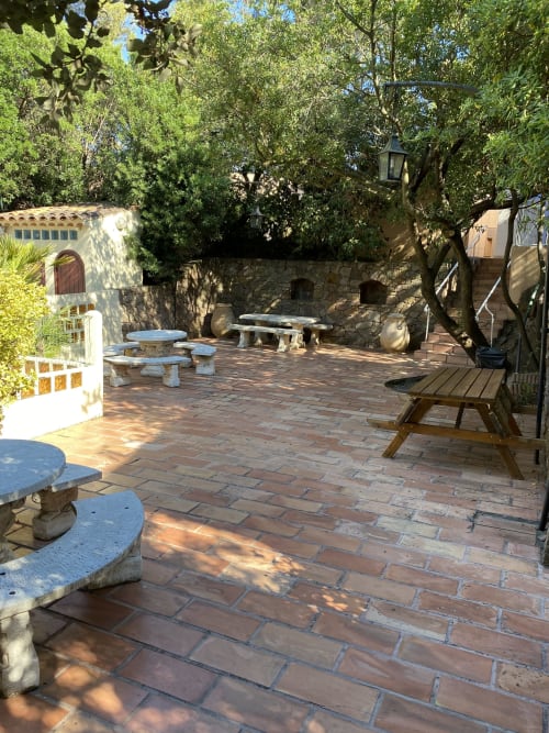 Cour ombragée du Camping La Lézardière avec terrasse en terre cuite, sièges en pierre et arbres méditerranéens à La Valette du Var
