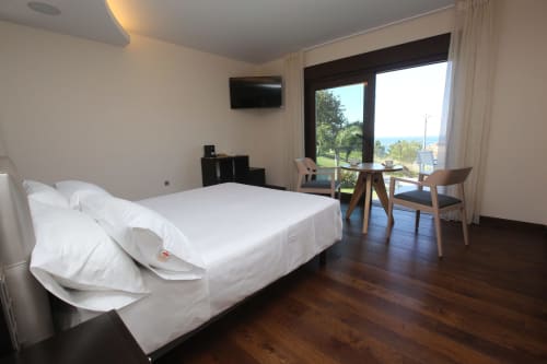 Amplia habitación de hotel en A Ballenera de Caneliñas con balcón vista al mar, cama queen, escritorio y servicios modernos en Cee