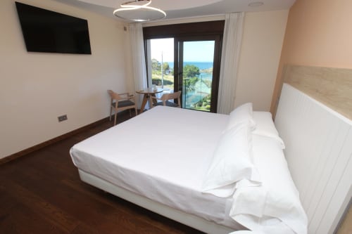 Habitación Lobeiro en A Ballenera de Caneliñas, Cee, con balcón con vista al mar, cama blanca, TV y mobiliario moderno