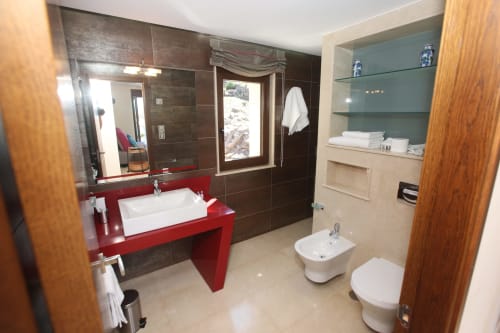 Baño moderno en habitación Lobeiro del hotel A Ballenera de Caneliñas, Cee, con tocador rojo, azulejos oscuros y accesorios blancos