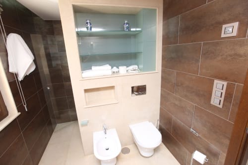 Baño moderno en la habitación Lobeiro del hotel A Ballenera de Caneliñas en Cee con paredes de azulejos marrones, sanitarios blancos y