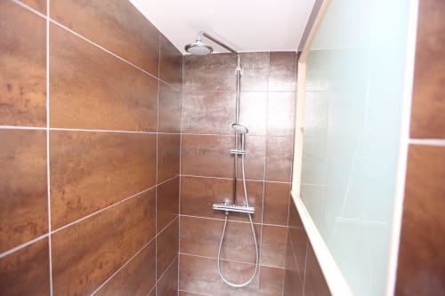 Moderno baño con azulejos marrones y alcachofa de lluvia en la habitación Lobeiro del hotel A Ballenera de Caneliñas, Cee