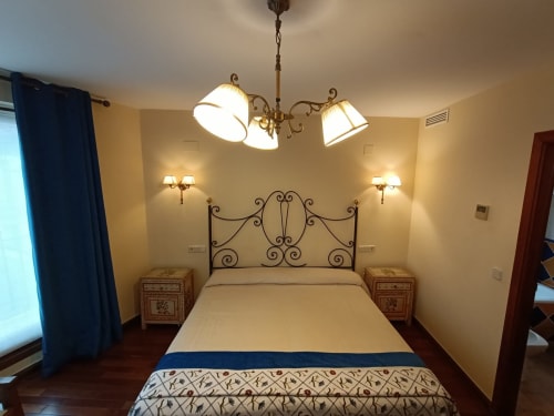 Dormitorio elegantemente decorado en La Posada Del Tietar con cama de hierro forjado, iluminación cálida y vistas a las montañas desde Santa María