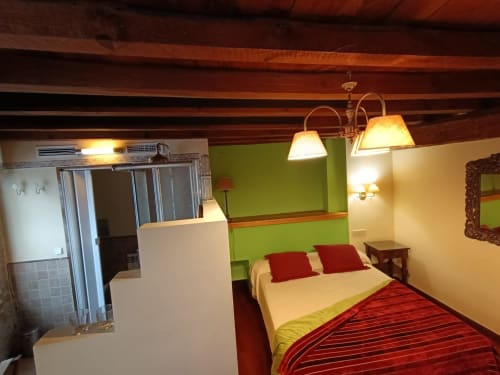 Acogedora habitación en La Posada Del Tietar con pared de acento verde lima, ropa de cama roja, vigas de madera vista e iluminación cálida