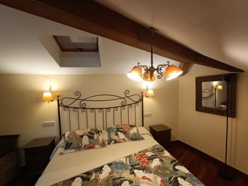 Acogedora habitación en la buhardilla de La Posada Del Tietar con cama de hierro ornamentada, iluminación cálida y techo de madera inclinado
