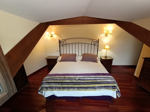 Acogedor dormitorio en buhardilla de La Posada Del Tiétar con cama de hierro forjado, vigas de madera e iluminación cálida en Santa María del Tiétar