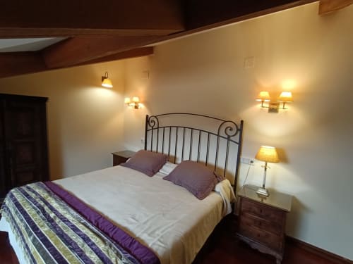 Acogedora habitación en La Posada Del Tiétar con cama de hierro forjado, iluminación cálida y vigas rústicas de madera en Santa María del Tiétar