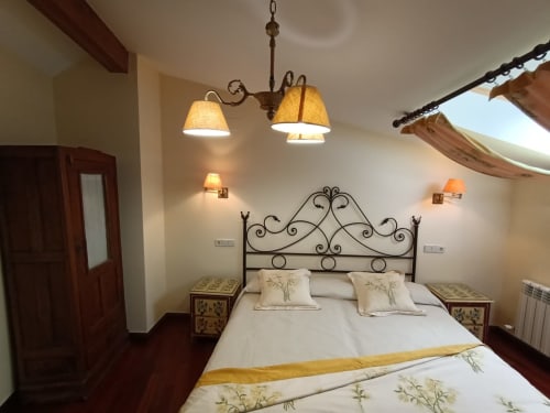 Elegante habitación en La Posada Del Tietar con cama de hierro forjado ornamentado, lámparas gemelas y decoración tradicional española