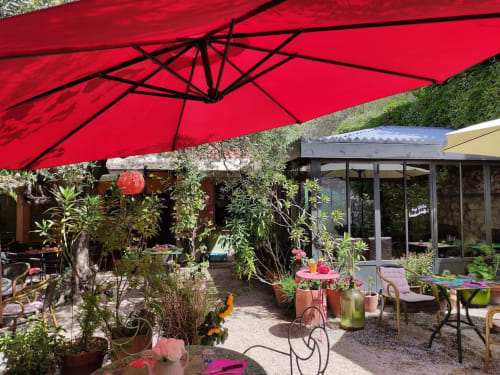 Roter Schirm spendet Schatten über die üppige Gartenterrasse des La Bouscatière in Moustiers-Sainte-Marie