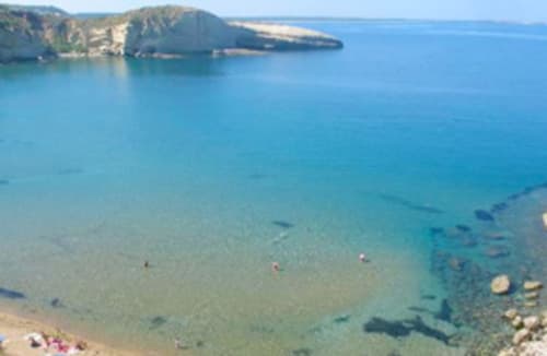 Acque turchesi trasparenti e spiaggia sabbiosa a Torre Grande Oristano, con scogliere rocciose e bagnanti, perfetto per il fronte spiaggia