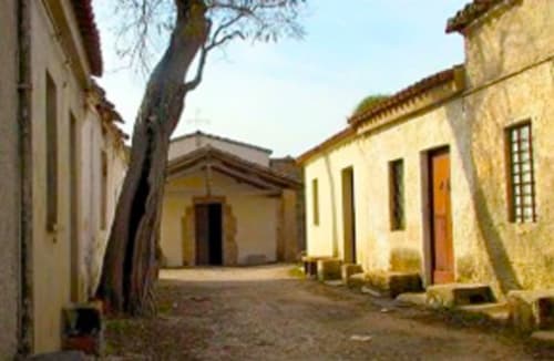 Patio rústico con edificios de piedra y puerta de madera en Affittacamere Al Mare en Torre Grande, Oristano