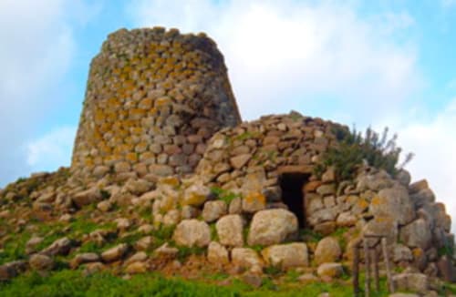 Ruinas de una antigua torre de piedra cerca de Torre Grande, Oristano, con entrada abovedada y rocas apiladas contra el cielo azul
