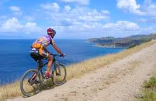 Radfahrer fährt entlang der Küstenklippen bei Torre Grande Oristano mit dem blauen Mittelmeer und Inseln im Hintergrund
