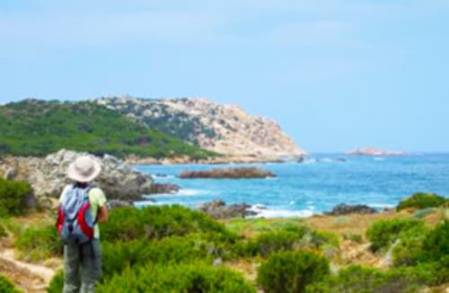 Wanderer mit rotem Rucksack blickt auf das türkisfarbene Mittelmeer und die felsige Küste bei Torre Grande, Oristano