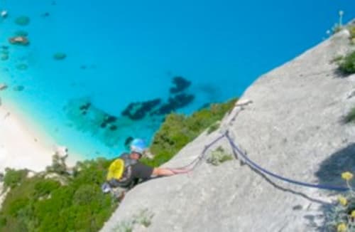 Wanderer mit gelbem Rucksack auf felsiger Klippe mit Blick auf türkisfarbenes Meer bei Torre Grande Oristano