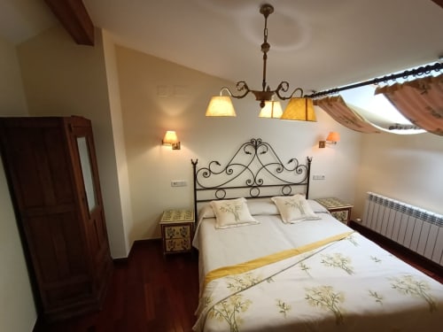 Elegante habitación de La Posada Del Tiétar con cama de hierro ornamentada, ropa de cama crema, iluminación cálida y muebles rústicos