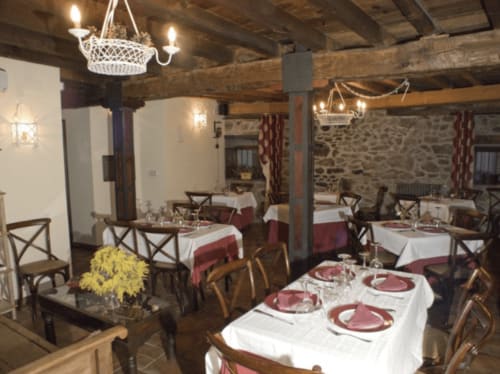 Comedor rústico en La Posada Del Tietar con vigas vistas, lámpara de araña y mesas elegantemente preparadas en blanco y borgoña
