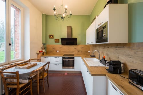 Cuisine moderne avec placards blancs, plan de travail en bois et murs vert citron au cottage L'âtre du Château de la Malmaison