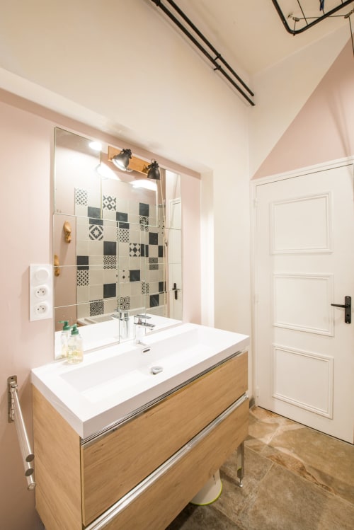 Salle de bain moderne au Château De La Malmaison avec meuble vasque en bois, lavabo blanc, douche carrelée à motifs et murs rose