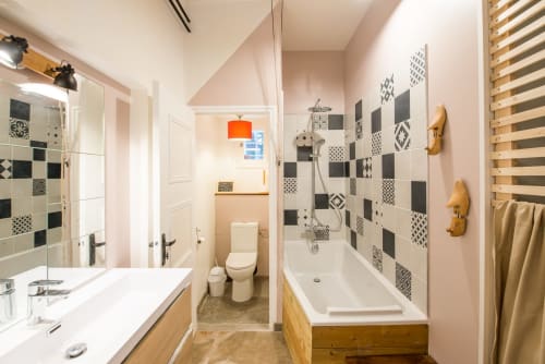 Salle de bain moderne aux murs roses, carrelage noir et blanc, meuble-lavabo en bois, baignoire et douche au Château de la Malmaison