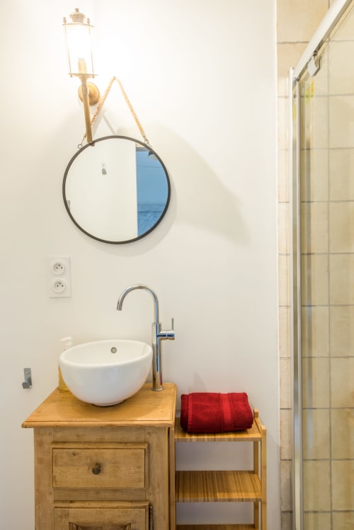 Salle de bains moderne du gîte L'atelier de Perrine au Château de La Malmaison Aÿ, avec miroir rond, vasque et serviettes rouges
