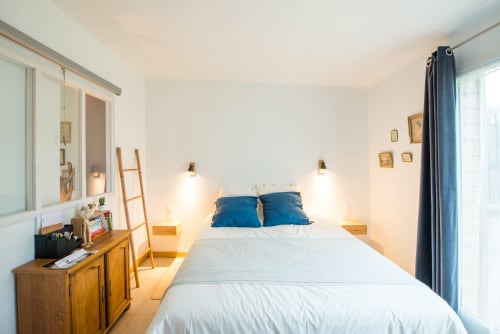 Chambre lumineuse du gîte Château De La Malmaison en Champagne avec lit blanc, oreillers bleus, mobilier en bois et jardin
