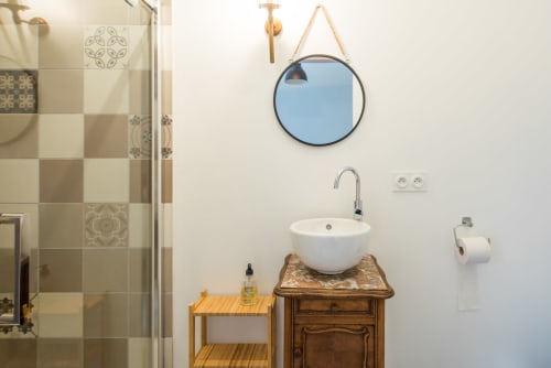Salle de bain moderne du Château de la Malmaison avec miroir rond, vasque blanche sur meuble en bois et cabine de douche
