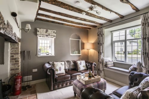 Luxury cottage sitting area with exposed beams, leather Chesterfield sofa, arched mirror, large windows, and patterned