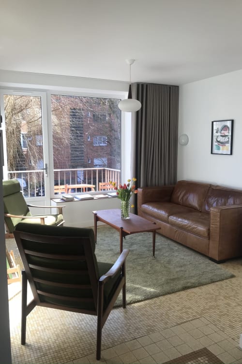 Salon moderne avec canapé en cuir, fauteuils vintage et vue sur la ville au gîte Le Gite Moderne à Dunkerque