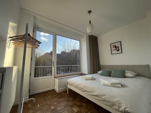 Chambre moderne au Gite Moderne à Dunkerque avec balcon, lit blanc, coussins verts et vue sur les montagnes