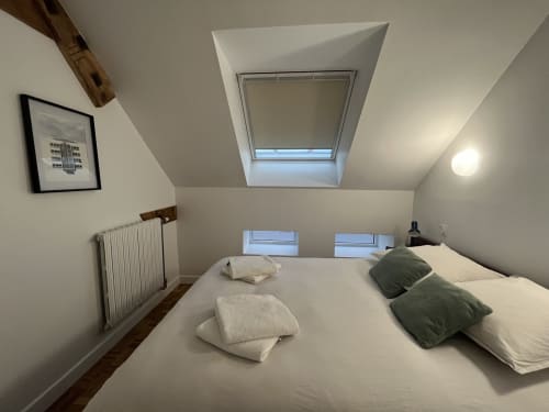 Chambre mansardée moderne au Gité Moderne à Dunkerque avec velux, literie blanche, coussins verts, radiateur et vue sur la ville.