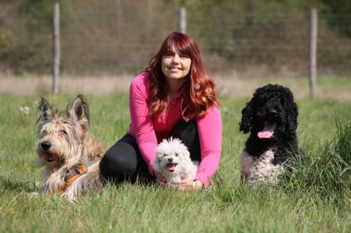 Femme aux cheveux roux accroupie avec trois chiens dans un champ herbu au Domaine Des Bois Argentés B&B à Pruniers-en-Sologne