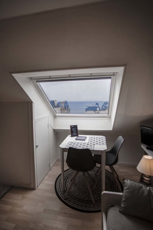 Espace de travail avec puits de lumière offrant une vue sur la mer de Saint-Malo à la Résidence Le Roc Fleuri, avec bureau, chaise noire et tapis à motifs