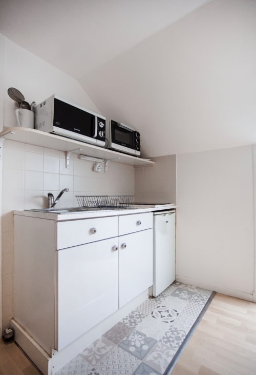 Kitchenette compacte à la Résidence Le Roc Fleuri à Saint-Malo avec meubles blancs, évier, micro-ondes et plaque de cuisson